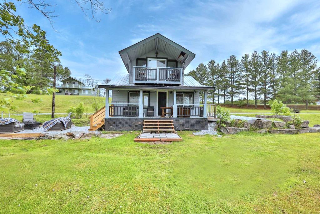 The Jigged Cabin exterior with covered porch, balcony, and grassy waterfront lawn.