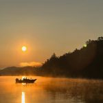Angler fishing at sunrise on Lac Heney with golden morning mist over the water.